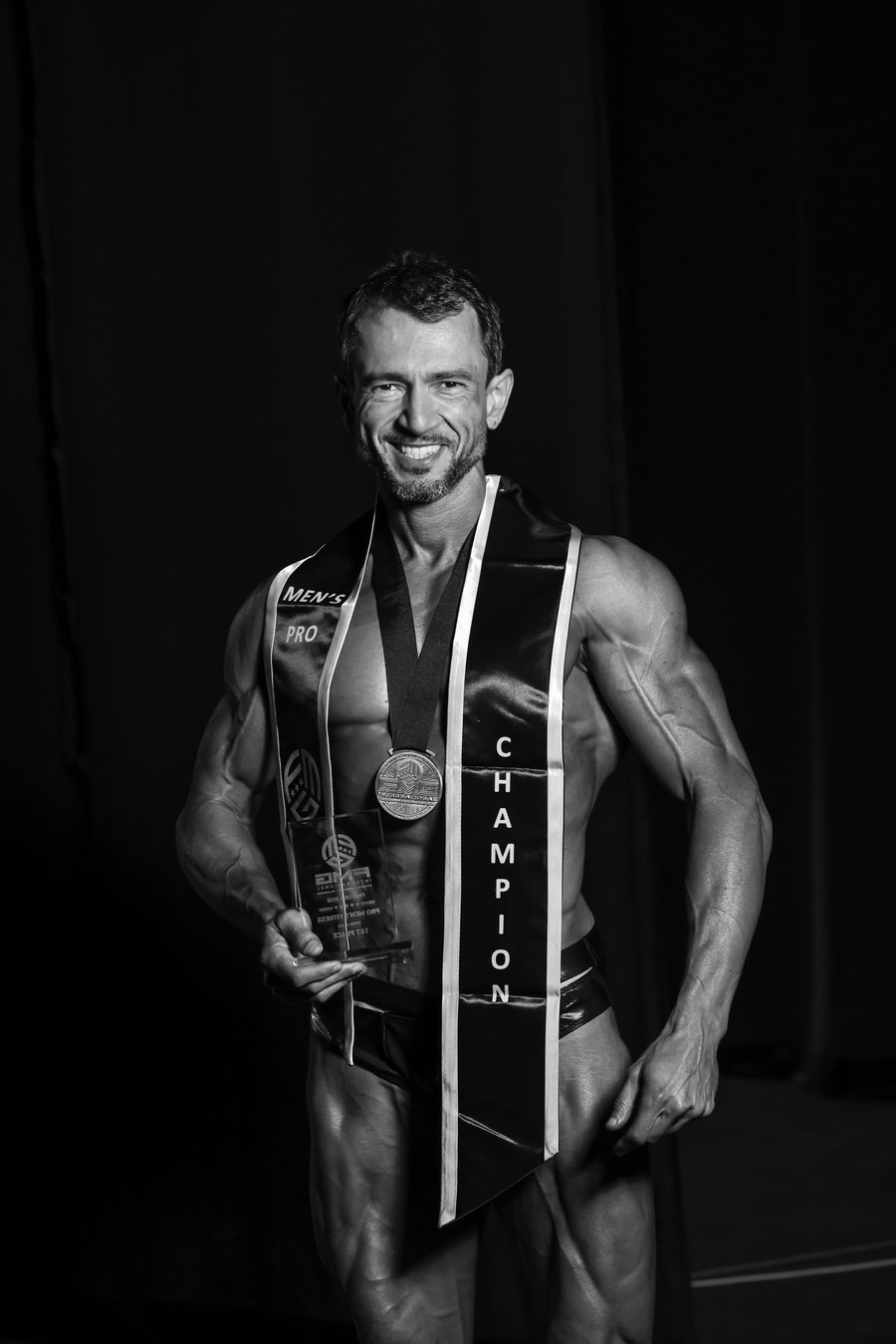 A champion holds his medal, trophy and sash backstage